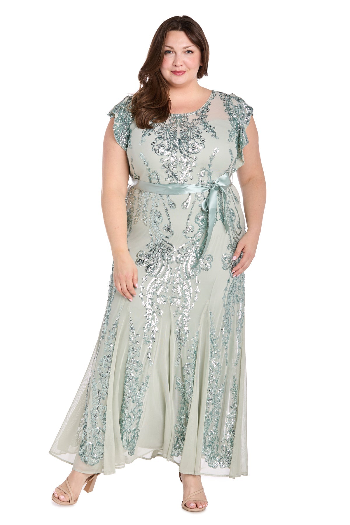 A woman stands facing forward, hand by her side, wearing the Plus-Size Sage Green Formal Dress: R&M Richards 3465W—floor-length with sequin print and a satin ribbon belt—against a white background.